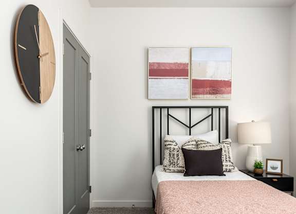 A bedroom with a bed, nightstand, lamp, and a clock on the wall.
