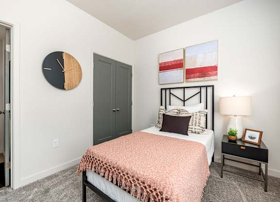 A bedroom with a bed, nightstand, and a clock on the wall.