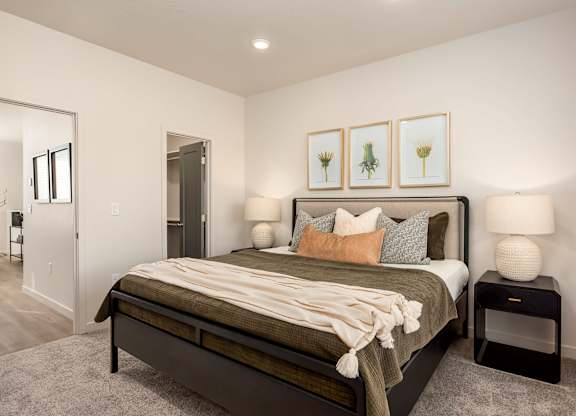 A bedroom with a bed, nightstands, and framed pictures on the wall.