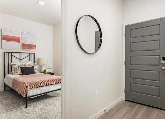 A bedroom with a bed, pillows, a round mirror, and a grey door.