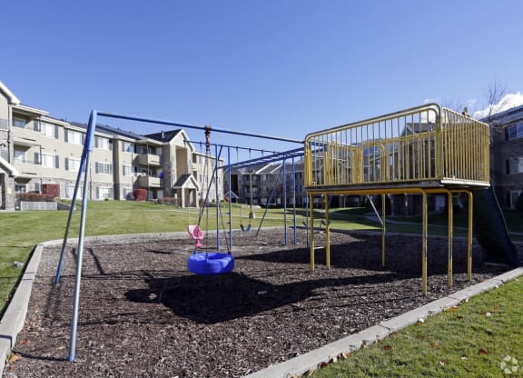a playground with a swing set and playset in front of an apartment building
