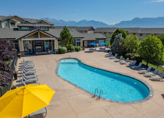 our resort style swimming pool with lounge chairs and a yellow umbrella at Aldara Apartments in Saratoga Springs, Utah