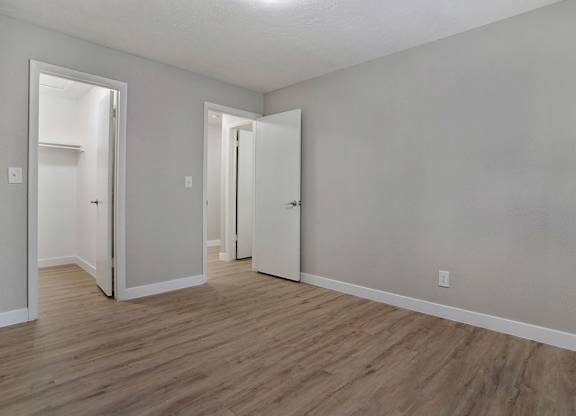 A room with white walls and wooden flooring with three open doors.
