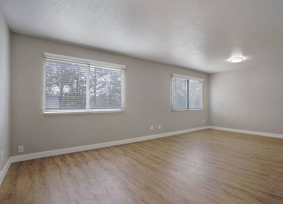 A room with wooden flooring and two windows.