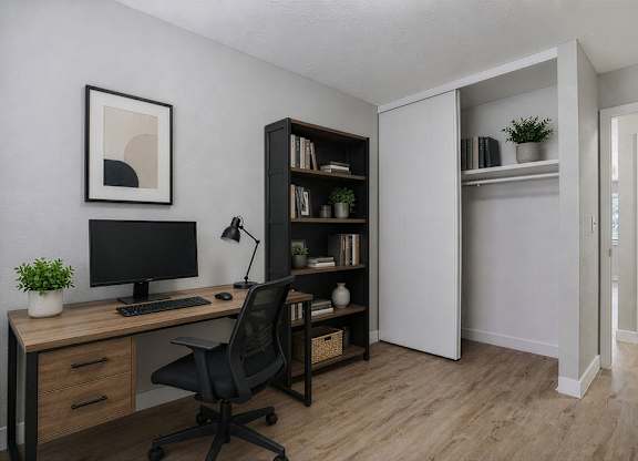 A black chair is in front of a desk with a computer and a plant.