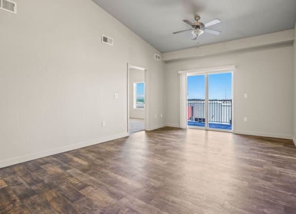 an empty living room with a ceiling fan and a balcony