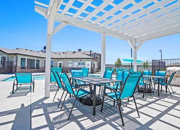 A white pergola with blue chairs and a table is set up on a patio.
