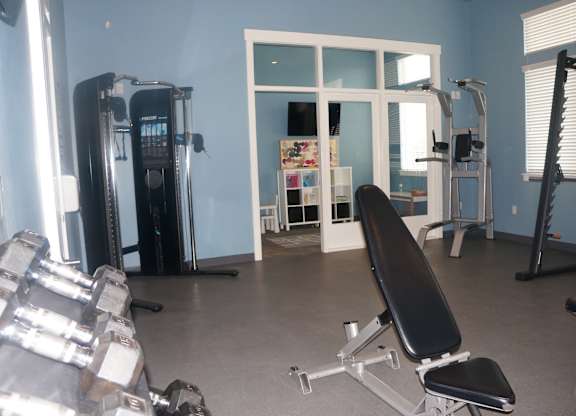 A gym with a variety of equipment including dumbbells, a bench, and a squat rack.