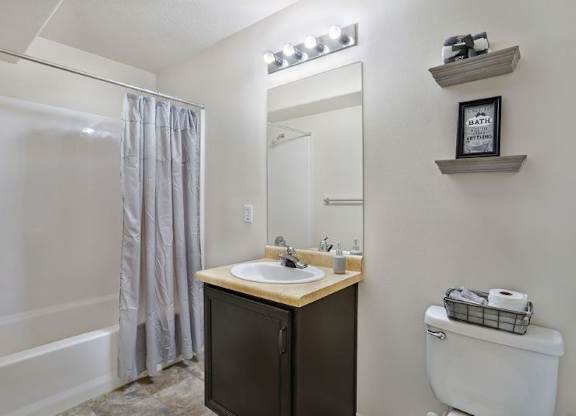 A bathroom with a white toilet, a sink with a black cabinet, and a shower with a grey curtain.