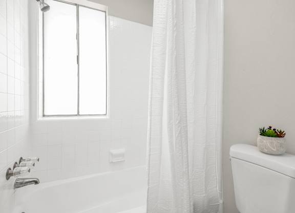 A white bathroom with a tub, toilet, and a window.