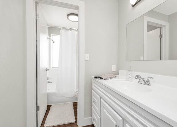 A white bathroom with a sink, mirror, and shower.