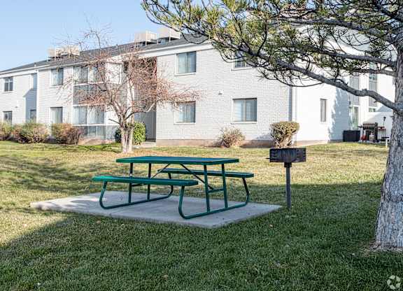A green picnic table sits in front of a grey building.