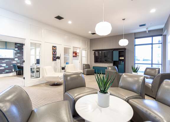 A white table with a plant on it sits in the middle of a room with grey couches.