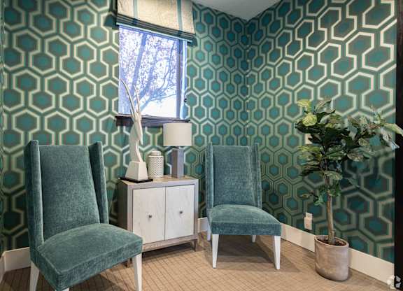 Two green chairs sit in front of a patterned wallpapered wall.