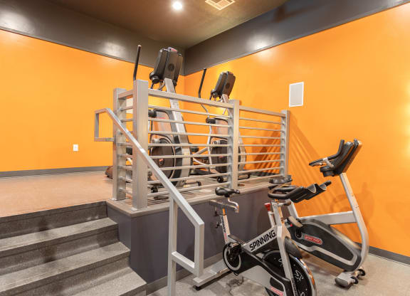 a gym with exercise equipment, ellipticals, and stairs in a building with orange walls at Outlook Apartments for rent in Springville and Provo, UT.