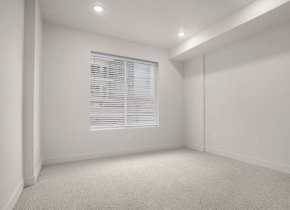A room with a window covered by blinds and carpeted floor.