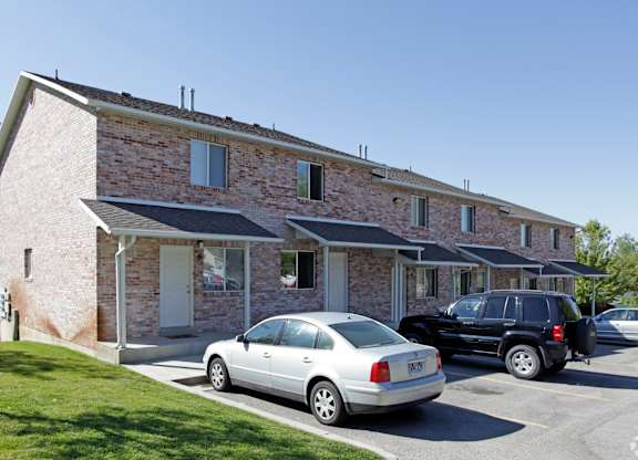 A silver car is parked in front of a house with a black car behind it.