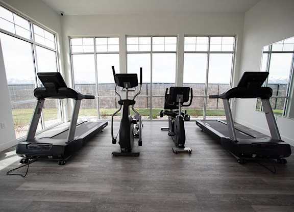 A row of treadmills and exercise bikes are lined up in a brightly lit room.