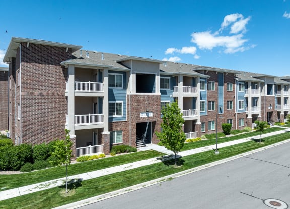 an apartment building on a city street with grass and trees at Outlook Apartments for rent in Springville and Provo, UT.