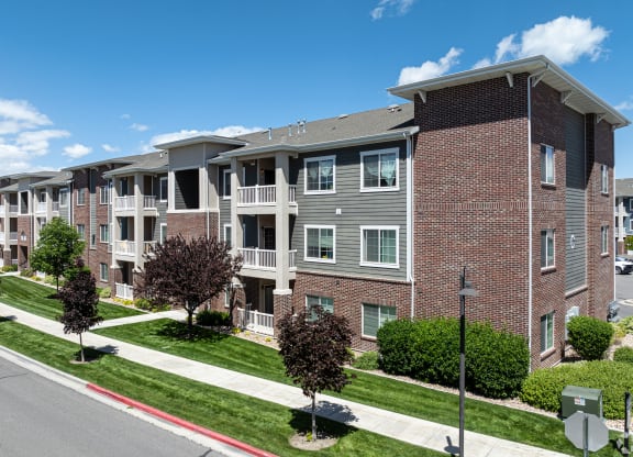 an apartment building on a city street with grass and trees at Outlook Apartments for rent in Springville and Provo, UT.