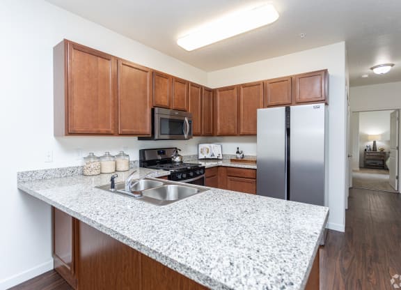 a bright kitchen with a granite counter top and a stainless steel refrigerator at Outlook Apartments for rent in Springville and Provo, UT.