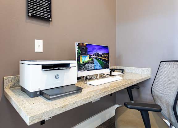A HP printer sits on a desk next to a monitor and a chair.