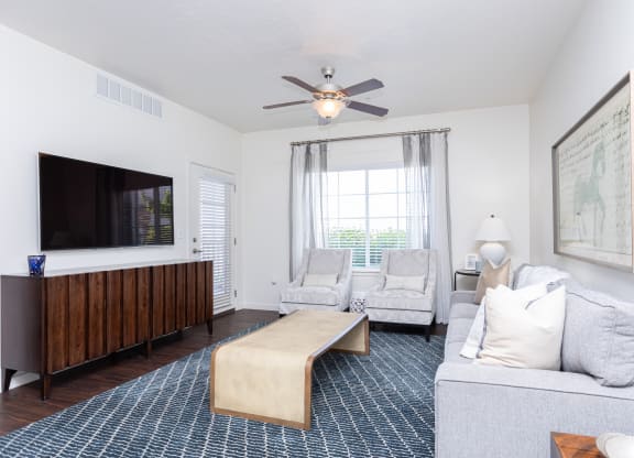 a bright living room with a ceiling fan and a tv at Outlook Apartments for rent in Springville and Provo, UT.