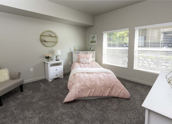 a bedroom with gray carpeting and a bed with a pink comforter