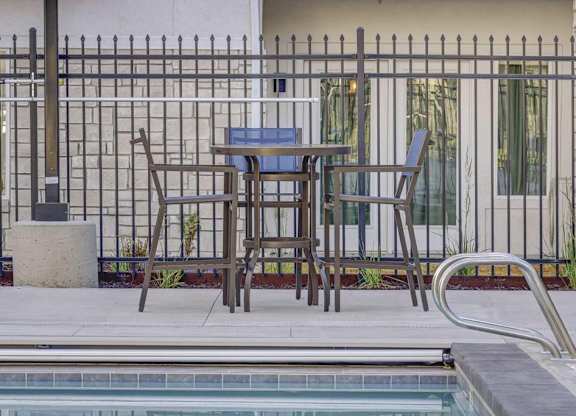 A poolside table with two chairs is set up next to a pool.
