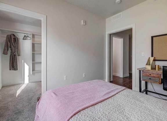 A bedroom with a pink bedspread and a wooden dresser.