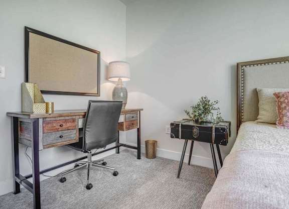 A bedroom with a bed, desk, chair, and lamp.