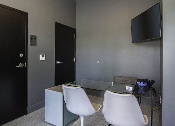 A black door is on the left of a room with a glass table and two white chairs.