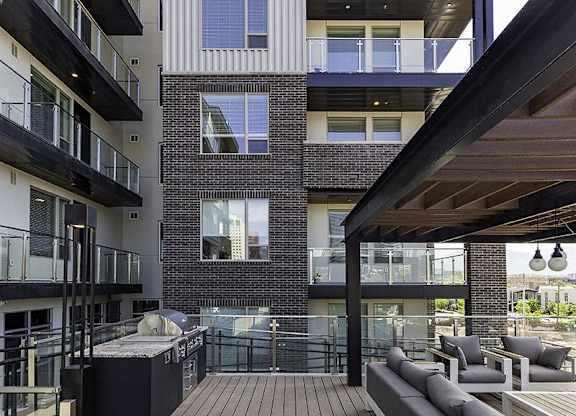A modern balcony with a table and chairs is attached to a brick building.