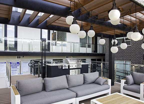 A modern outdoor seating area with grey couches and wooden tables.