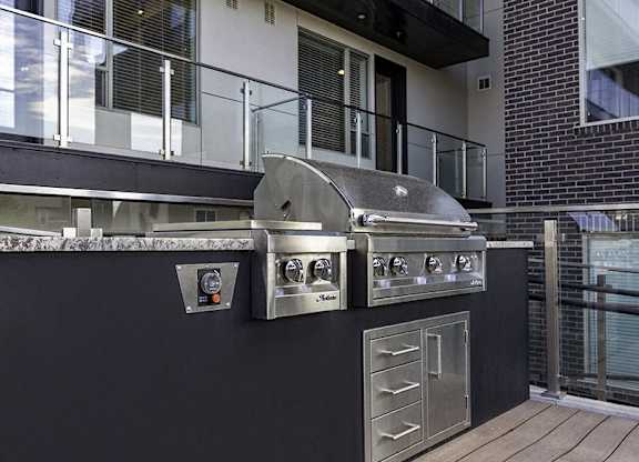 A stainless steel outdoor grill with a side burner and a drawer is on a black countertop.