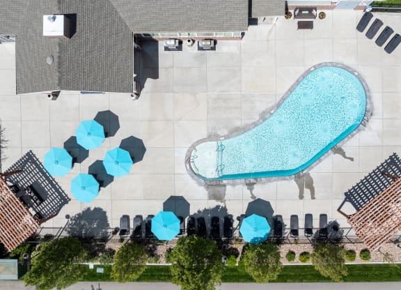an aerial view of a pool with blue umbrellas and a poolside building at Outlook Apartments for rent in Springville and Provo, UT.