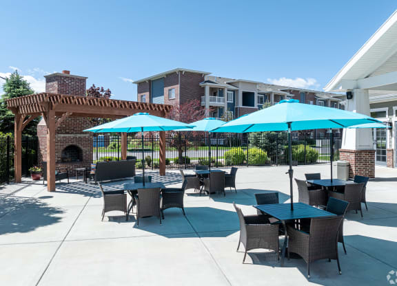 a patio with tables and umbrellas in front of a building at Outlook Apartments for rent in Springville and Provo, UT.
