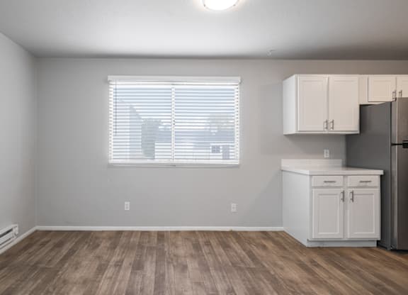 A kitchen area with a refrigerator, cabinets, and a window with blinds.