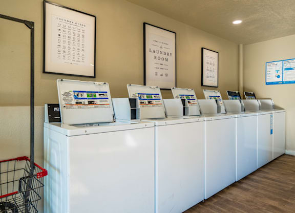 A laundry room with a row of washing machines and a shopping cart.