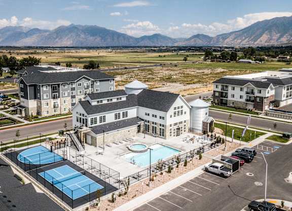 A large building with a pool and tennis courts in front of it.