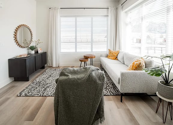 A living room with a grey sofa, a wooden table, and a mirror on the wall.