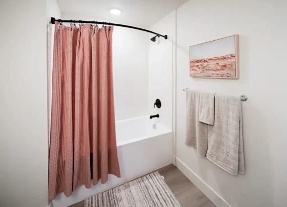 A bathroom with a pink shower curtain and a white bathtub.