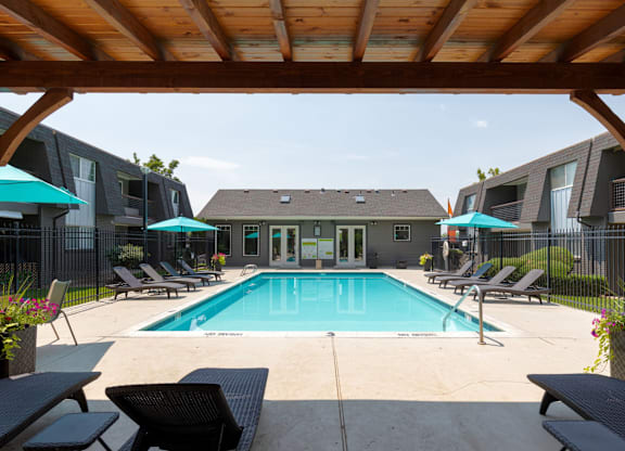 A pool area with a wooden pergola and lounge chairs.