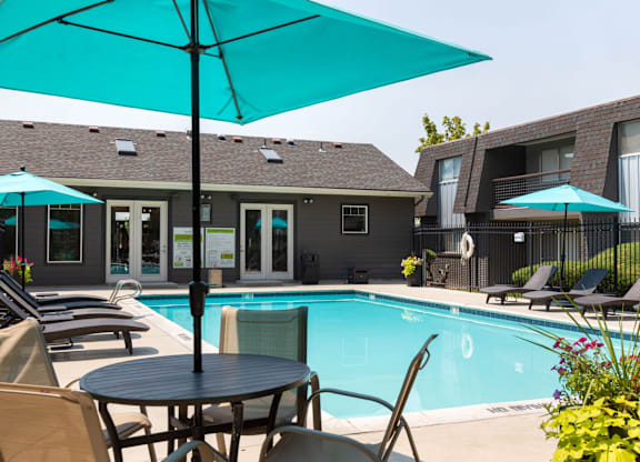 A pool area with a table and chairs and umbrellas.