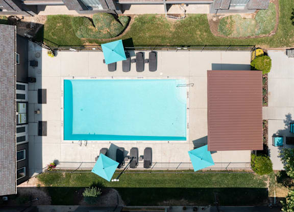 A swimming pool surrounded by chairs and a brown building.