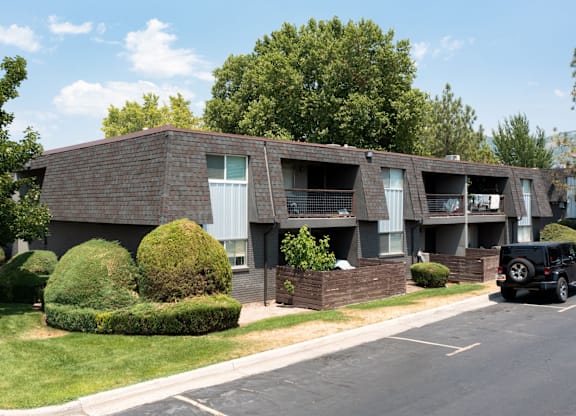A black car is parked on the street in front of a brick apartment building.