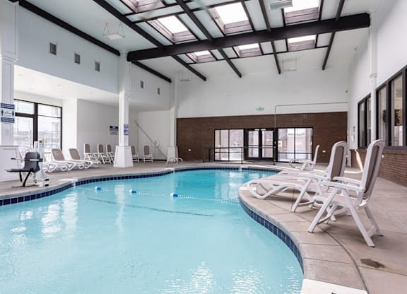 A large indoor swimming pool with lounge chairs and a skylight.