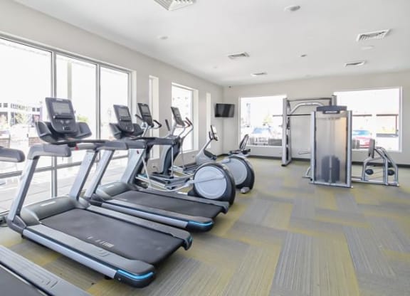 a gym with a row of cardio equipment and windows