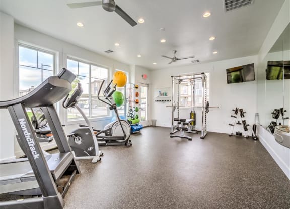 a gym with various exercise equipment and windows at Aderra apartment complex in Roy, Utah