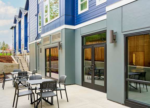 A patio with a table and chairs is outside a blue and grey building.